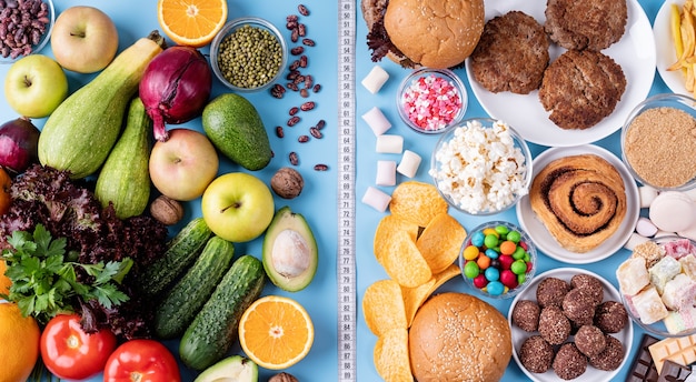 Photo fruit and vegetables vs sweets and fast food top view flat lay on blue background