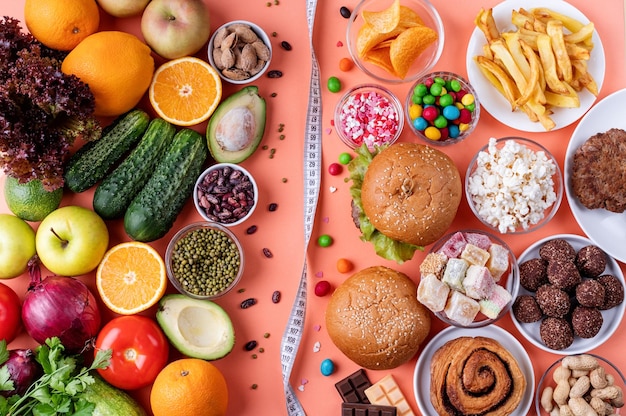 Fruit and vegetables vs sweets and fast food top view flat lay on orange background