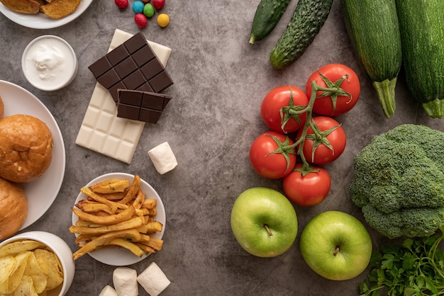 Fruit and vegetables vs sweets and potato fries top view flat lay on dark table