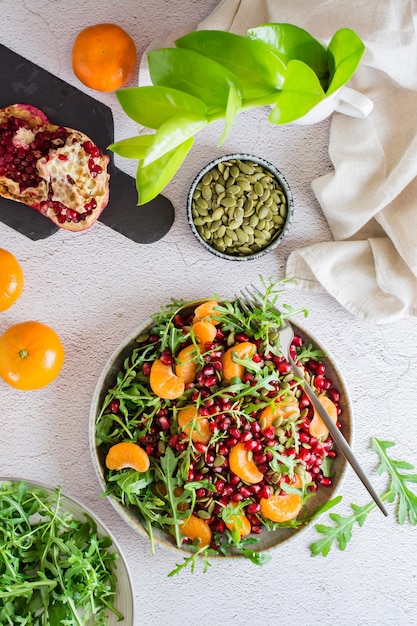 Fruit vitamin salad of pomegranate, tangerine, arugula and pumpkin seeds in a plate on the table. Organic vegetarian food.  Top and vertical view.