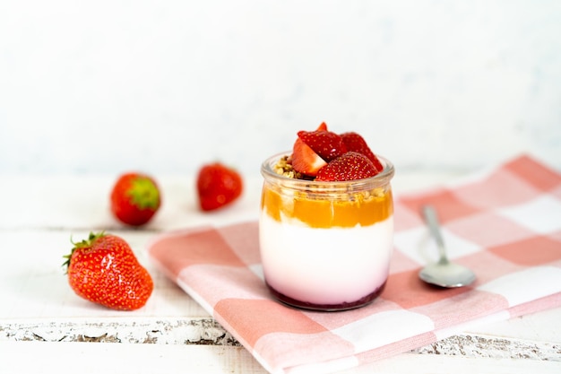 Fruit yogurt berry with muesli and fresh strawberries on a white wooden background