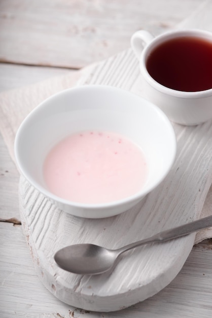 Fruit yogurt and cup of tea on the white wooden table