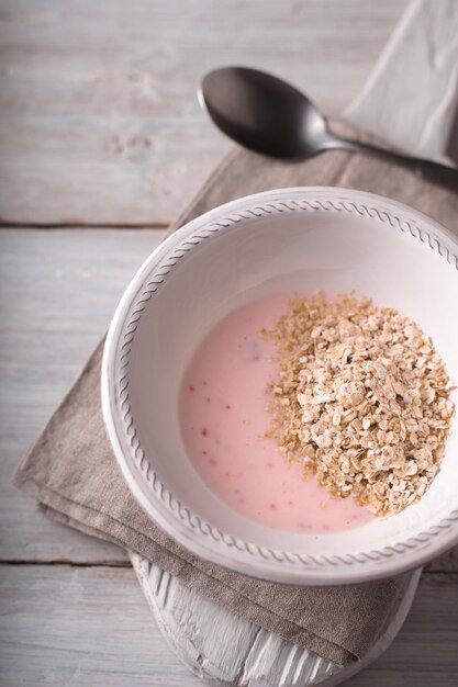 Fruit yogurt with oak flakes on the white wooden table vertical