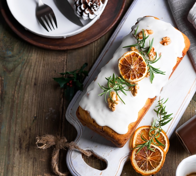 Fruitcake bestrooid met suikerglazuur, noten en droge sinaasappel op oude houten. kerst- en wintervakantie zelfgemaakte cake