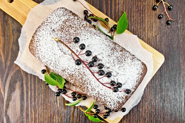 Fruitcake bird cherry with berries on a paper on the background of the wooden board top