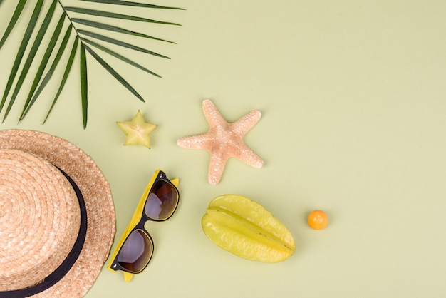 Fruitcarambol, strandaccessoires en gebladerte van een tropische plant op gekleurd papier. Zomerachtergrond met zeesterren en fruit