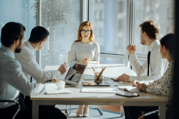 Fruitful collaboration. Charming female boss sitting at the head of the table with her employees and developing a project plan together with them