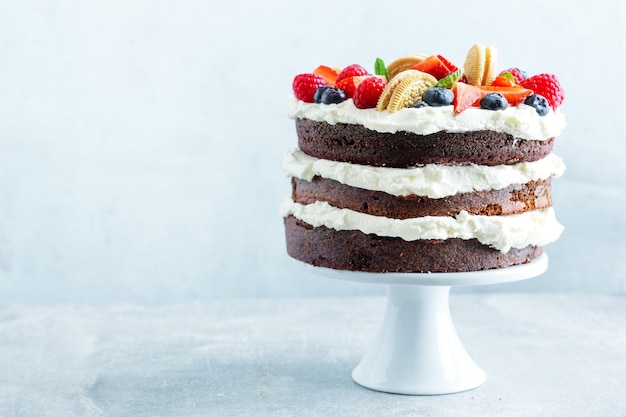 Fruitige cake met vers fruit en room op stander op lichte achtergrond.