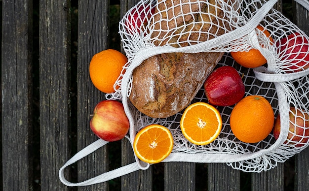 Fruits and bread in a shopping bag on a wooden background