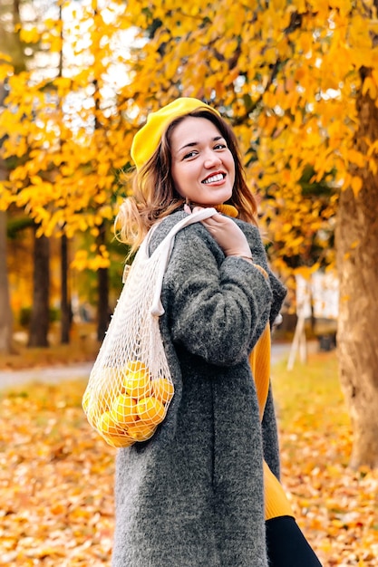 Fruits lemons in an ECO bag on the shoulder of a young woman in a gray polto and a sweater