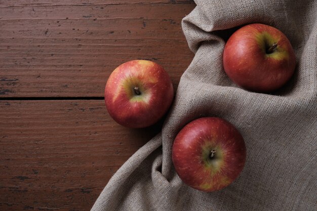 Fruits in a linen tablecloth on a old wooden table Apples on a dark red background