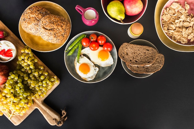 Photo fruits, muesli, fruits and fried omelette with tomatoes and peas on black background