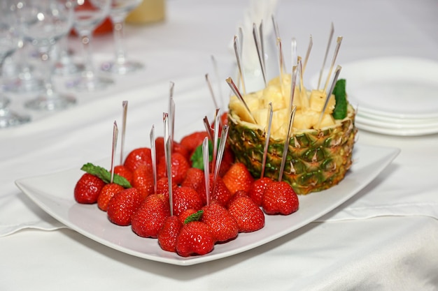 Fruits on a plate in a restaurant fruits for a buffet table red strawberries on skewers on a stick pineapple cut into pieces