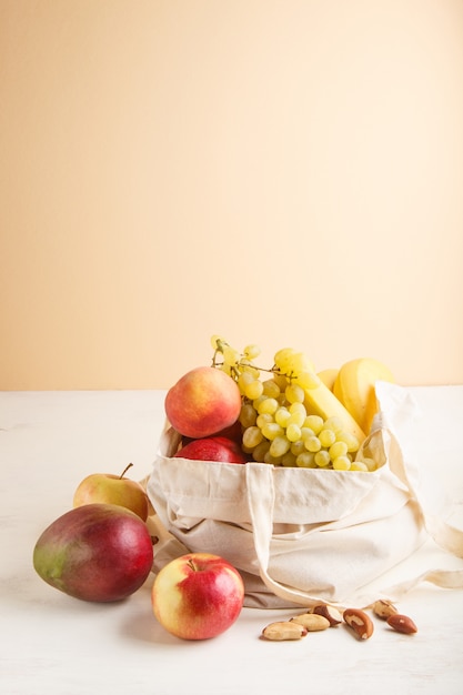 Fruits in reusable cotton textile white bag on white wooden . Zero waste shopping, storage and recycling . Side view, copyspace. 