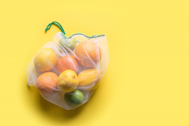 Foto frutta in sacchetti riutilizzabili ecologici a rete su giallo.