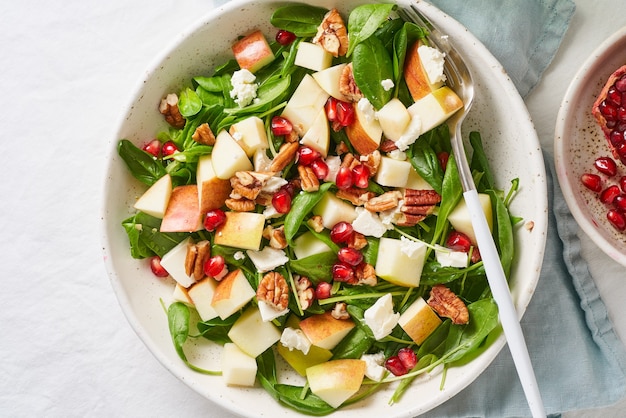 Insalata di frutta con noci, cibo equilibrato, mangiare pulito. spinaci con mele, noci pecan e feta, guarniti con semi di melograno in una ciotola sul tavolo con tovaglia bianca.