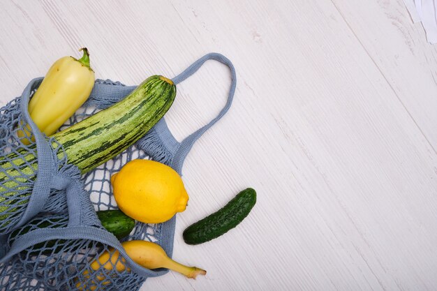 木製の背景の上のメッシュバッグの果物と野菜