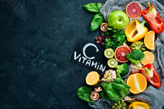 Fruits and vegetables that contain vitamin C Orange lemon apple roses garlic broccoli apple kiwi spinach Top view On a black stone background