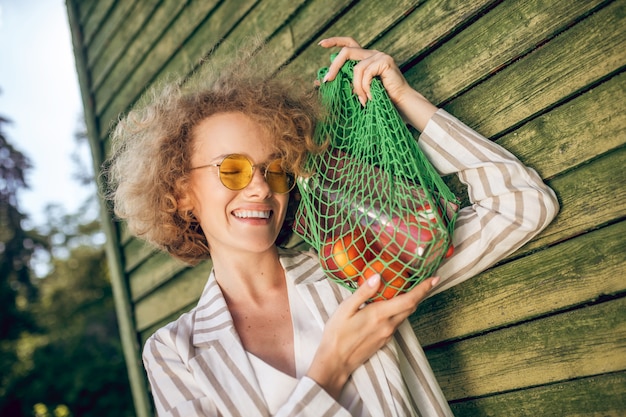 Фрукты. Молодая женщина в солнцезащитных очках держит сетку с фруктами