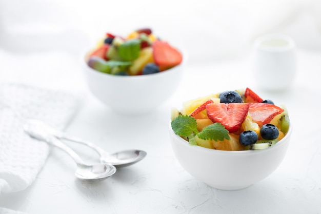 Fruitsalade met aardbeien, kiwi, abrikozen en bosbessen in witte borden op een witte tafel