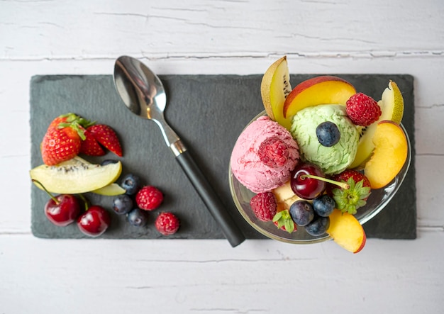Foto fruitsalade met bolletje vanille-ijs aardbei pistache in een kom op een stuk leisteen is