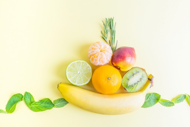 Fruitschaal - banaan, kiwi, mandarijn, nectarine, limoen - op pastelkleurig geel.