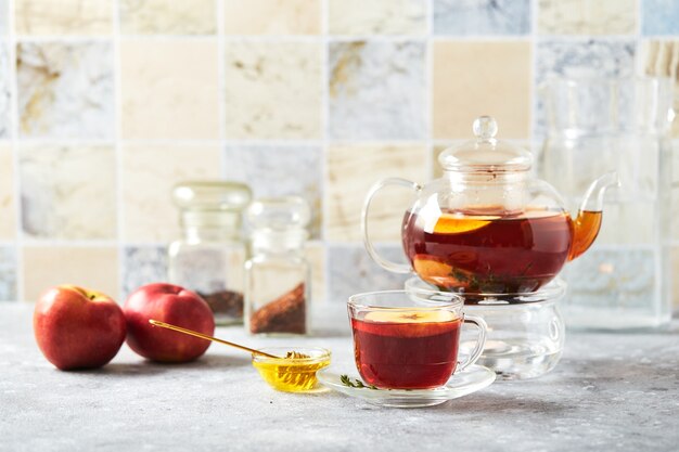 Fruitthee met appels en tijm in glazen theepot en kopje op de keukentafel