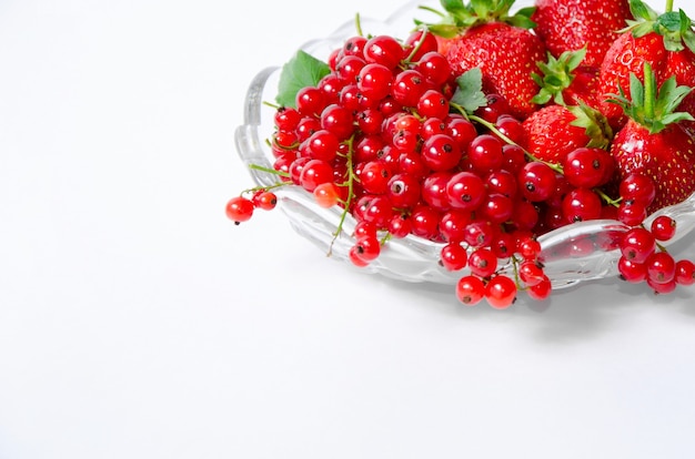 Fruitvaas met aardbeien en rode aalbessen op een witte achtergrond in de rechterbovenhoek van het frame.
