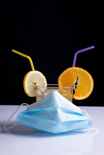 Fruity coronavirus cocktail in protective mask concept on white table and black background