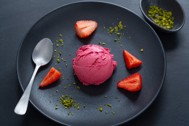 Fruity strawberry Ice cream scoops with strawberry sauce served on plate with fruits and pistacchios. Top View.