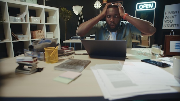 Photo frustrated african american guy checking project result online in dark office