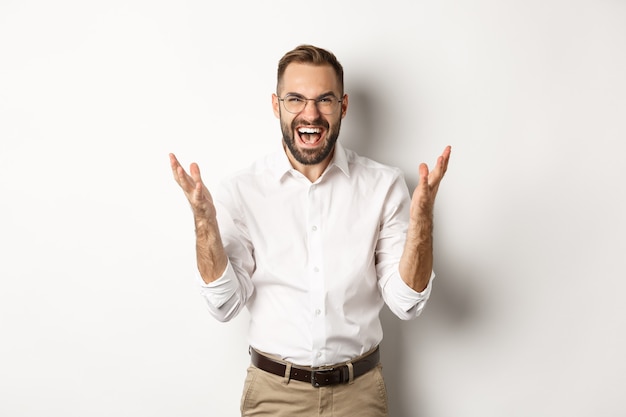 Frustrated and angry man screaming in rage, shaking hands furious, standing over white background. Copy space