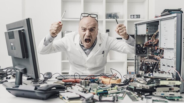 Frustrated angry technician trying to repair a computer his desk is full of computer parts