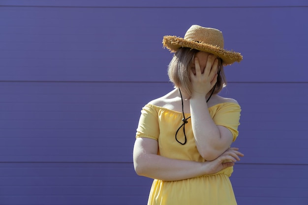 A frustrated Asian teen girl in a hat and dress covers her face with her hands Mental health
