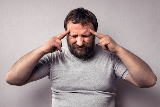 Frustrated bearded man touching his head with hands and keeping eyes closed