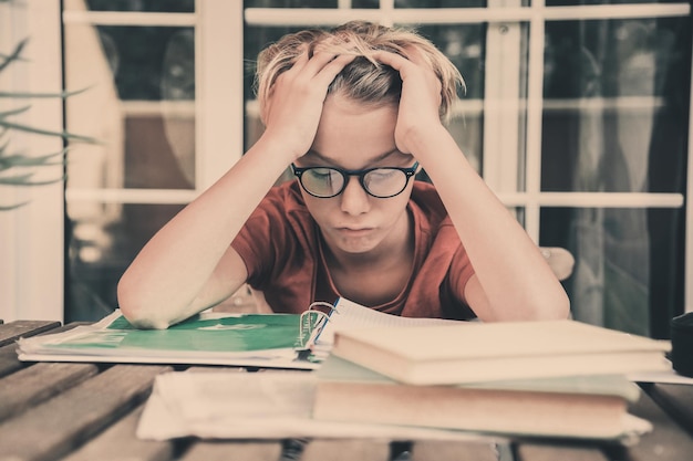 Photo frustrated boy siting next to books on desk at home