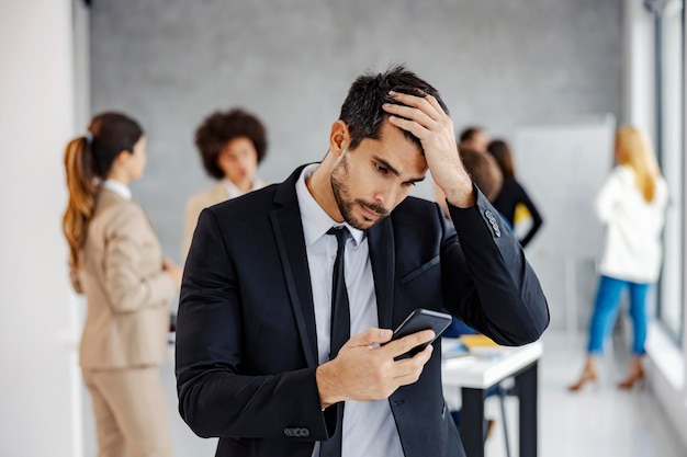 Разочарованный бизнесмен читает неудобное сообщение по телефону, стоя в офисе