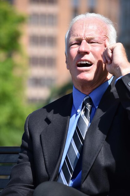 frustrated businessman touching forehead while sitting on bench in park