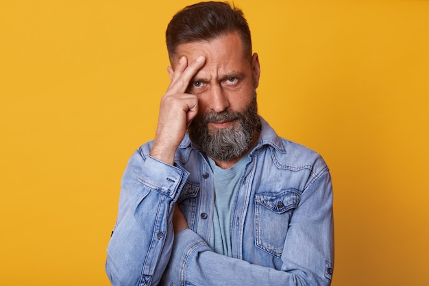 Frustrated confused handsome model posing emotionally, standing with crossed arms, holding one hand on face