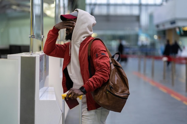 Frustrated disappointed African American male passenger with luggage overslept and missed flight