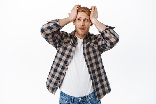 Photo frustrated and disappointed redhead man looking with sadness at upper left corner holding hands on head distressed feel bad and gloomy standing over white background