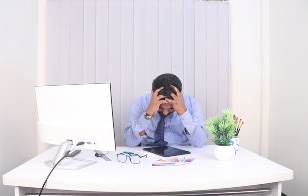 Разочарованный пожилой деловой человек, сидящий на столе с рукой за голову в офисе