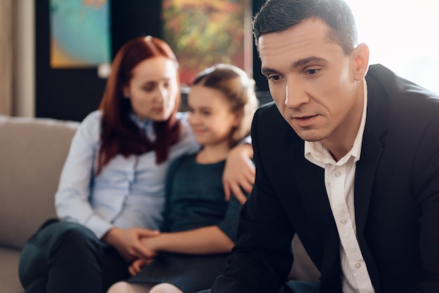 Frustrated father in suit sits on couch next to young wife.