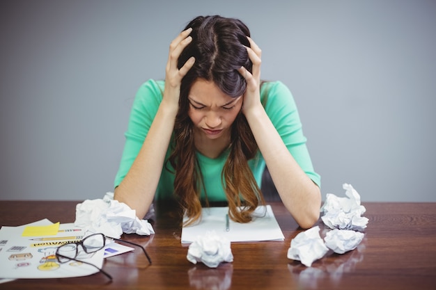 Frustrated female business executive sitting with crumpled papers balls