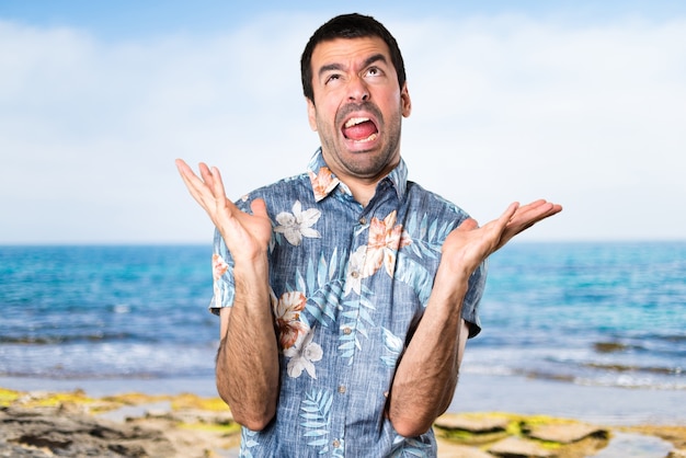 Foto uomo bizzarro frustrato con camicia di fiori sulla spiaggia