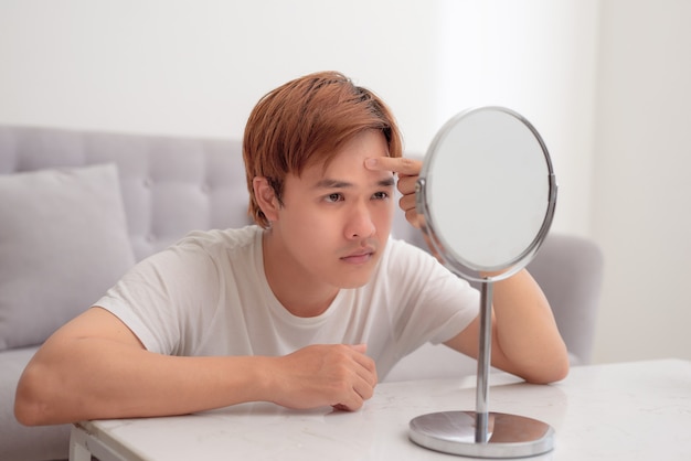 Frustrated handsome millennial guy concerned about facial skin problem