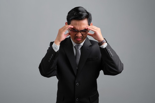 Frustrated handsome young businessman in formal suit suffering from headache because migraine isolated on grey background