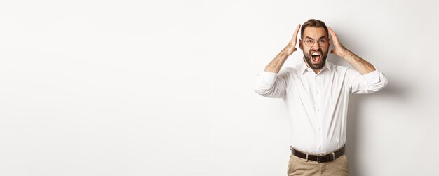 Frustrated man panicking shouting and looking anxious standing over white background