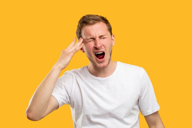 Frustrated man portrait. migraine pain. nervous guy yelling suffering from strong headache isolated on orange