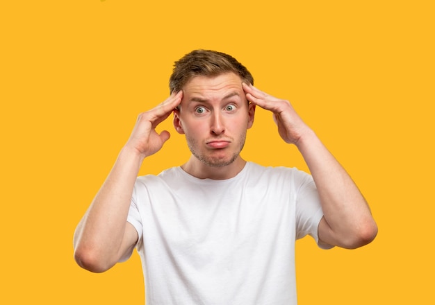 Frustrated man portrait. Panic attack. Stressed out guy touching head isolated on orange background.